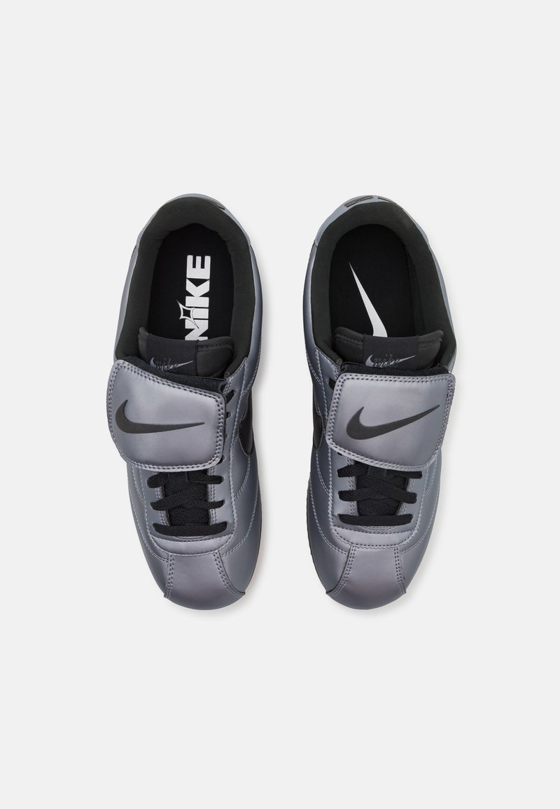 Zapatillas de cuero gris con cordones negros, una correa de Velcro y un interior negro que presenta el logo de Nike en la plantilla y en la lengua.