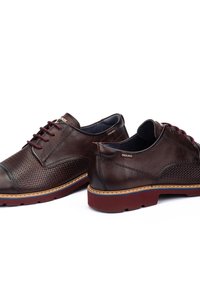 Bruine leren schoenen met een textuurpaneel en een gladde neus. Rode veters en accent op de zool. Logo aan de zijkant. Afgeronde vorm en gevoerde binnenkant.