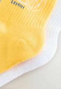 Yellow and white ankle socks with a ribbed texture. The yellow section features blue text reading "LEMON." Soft cotton blend material.