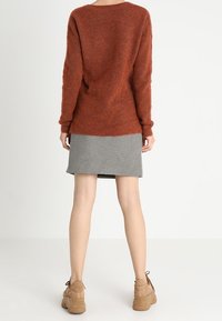 Pull couleur rouille à coupe décontractée, associé à une jupe à motif pied-de-poule noir et blanc. Chaussures avec semelles compensées beiges épaisses.