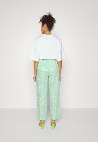 T-shirt oversized branca com mangas curtas, combinada com calças largas verdes estampadas com um design de ondas e sandálias de salto bloco verdes.