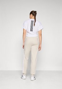 Biele skrátené tričko s čiernymi vertikálnymi pruhmi na chrbte, skombinované s béžovými nohavicami s bočnými bielymi pruhmi a čiernou obuvou.