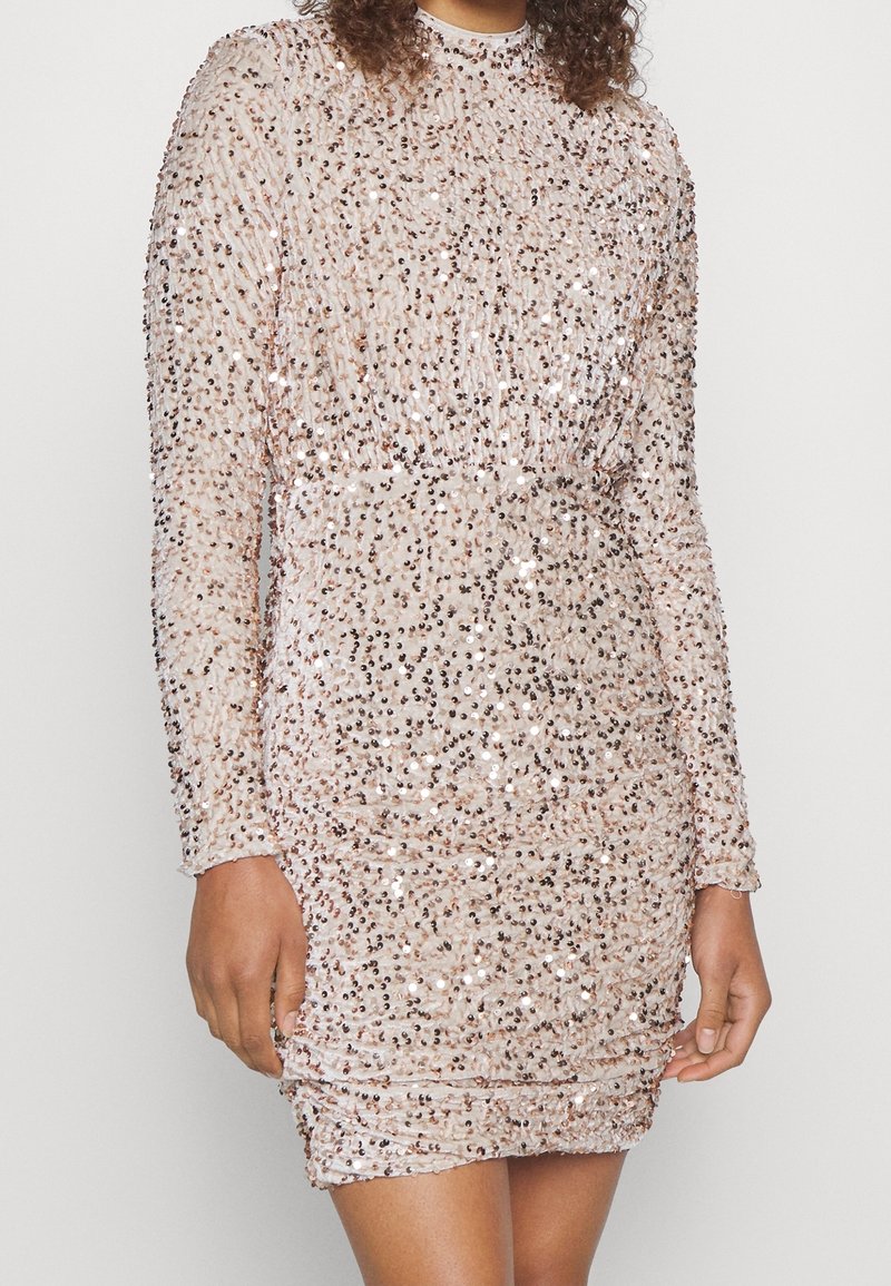 Kort klänning med lång ärm i pailletttyg i ljusrosa färg med rynkdetaljer som skapar en texturerad, skimrande effekt.