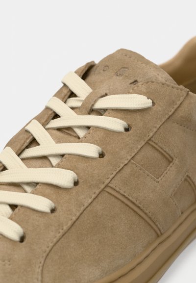 Beežist seemisnahast tennisejalanõu kreemvalgete paeltega, millel on tekstureeritud pealne, minimalistlik disain ja peene brändinguga külg.