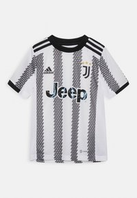 Maillot de football de la Juventus en blanc avec des motifs en triangles noirs. Présente des accents noirs, le logo Adidas, le marquage Jeep et trois étoiles jaunes.