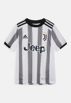 Maillot de football de la Juventus en blanc avec des motifs en triangles noirs. Présente des accents noirs, le logo Adidas, le marquage Jeep et trois étoiles jaunes.