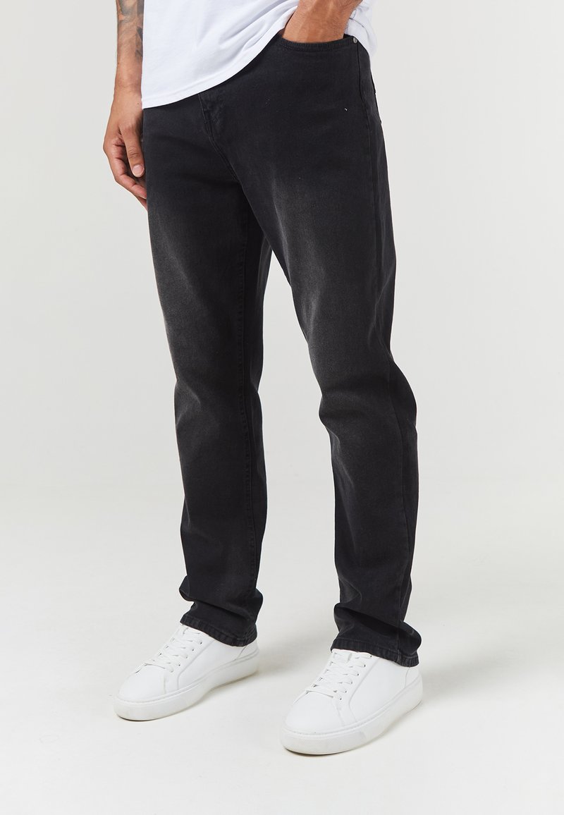Los jeans de mezclilla negros presentan un corte ajustado con una sutil textura desgastada, acompañados de zapatillas blancas para un look informal.