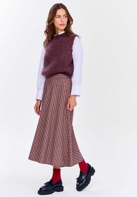 Bordový pletený bezsleeve svetr spárovaný s dlouhou skládací sukní s červeno-černým kostkovaným vzorem. Černé boty a červené ponožky.