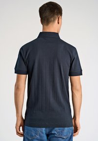 Ciemnoniebieska koszulka polo z krótkim rękawem i pionowym prążkowanym wzorem, z tradycyjnym kołnierzykiem i prostym dołem.