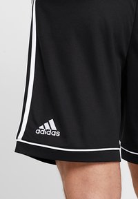 Mustat urheilushortsit, joissa on valkoiset sivuviivat, valmistettu kevyestä materiaalista ja joissa on pieni valkoinen Adidas-logo helman kohdalla.