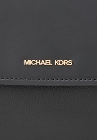 Portofel negru din piele texturată cu logo auriu „MICHAEL KORS”. Prezintă margini cusute și un finisaj neted. Formă dreptunghiulară compactă.