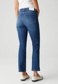 Jeans in denim con una vestibilità slim, vita media e leggermente svasati alla caviglia. Colore blu scuro con due tasche posteriori e un'etichetta bianca.