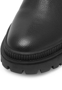 Čierna kožená členková obuv s textúrovaným povrchom, zaoblenou špičkou a hrubou gumovou podrážkou s hlbokým vzorom a rýhovanými akcentmi pozdĺž okraja.