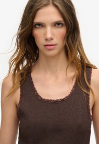 Brązowy rypsowy podkoszulek z koronkowym wykończeniem wokół dekoltu i otworów na ramiona. Posiada dopasowany krój i miękką teksturę.