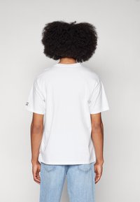 Tricou alb din bumbac cu mâneci scurte, guler rotund și un mic etichetă cu logo pe mâneca stângă. Croi lejer, textură fină. Jeanși din denim albastru deschis.