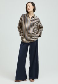 Striped shirt in beige and navy fabric with a relaxed fit, paired with navy wide-leg pants and pointed beige flats.