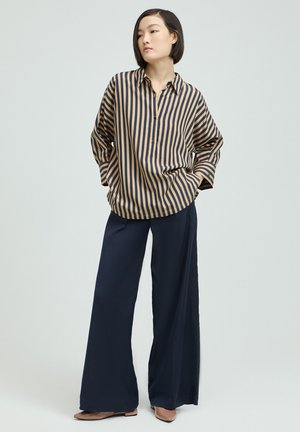 Striped shirt in beige and navy fabric with a relaxed fit, paired with navy wide-leg pants and pointed beige flats.
