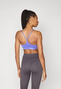 Μωβ αθλητικό σουτιέν με λεπτές τιράντες, διαθέτει ελαστική ταινία με λογότυπο. Συνδυάζεται με ψηλόμεσο σκουρογρί κολάν. Ομαλή υφή, αθλητική σχεδίαση.