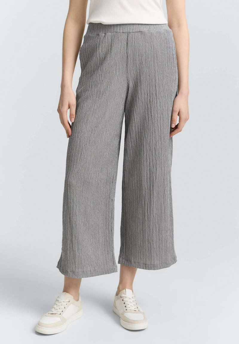 Pantalones de pierna ancha grises con plisados, cinturilla elástica y tejido texturizado, combinados con zapatillas blancas.