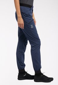Marineblauwe outdoor broeken met elastische boorden, zijzakken en een logo. Gemaakt van lichtgewicht materiaal met een gladde textuur.