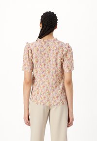 Blusa floreale a maniche corte con dettagli arricciati sulle spalle, caratterizzata da una palette di colori pastello che comprende rosa, giallo e viola su uno sfondo chiaro.