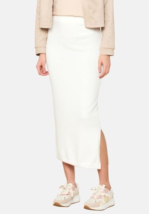 Frau trägt einen weißen Midirock mit seitlichem Schlitz, eine beige kurze Jacke und klobige weiße Sneaker mit pastellfarbenen Akzenten.