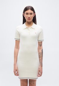 Πλεκτό φόρεμα πόλο σε  κρεμ απόχρωση με κοντά μανίκια, που διαθέτει υφασμάτινο μοτίβο, γιακά και μπλε λεπτομέρειες κατά μήκος των μανικιών και του τελειώματος.