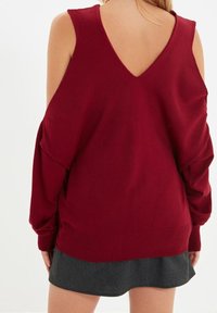 Bordowy sweter z długimi rękawami, dekoltem w serek na plecach i prążkowanym wykończeniem u dołu. Zestawiony z ciemnoszarą spódnicą o luźnym kroju i miękkiej fakturze.