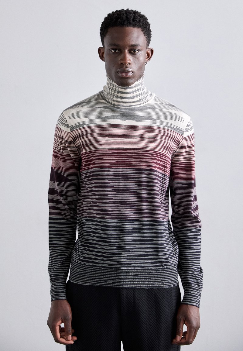 Juostuotas megztinis su aukštu kaklu, kuriame vyrauja pilkos, raudonos ir baltos spalvos, pagamintas iš minkštos mezgimo medžiagos, tvirtos konstrukcijos ir ilgomis rankovėmis.