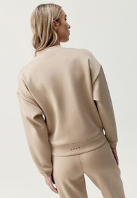 Beige sweatshirt med en avslappnad passform, med sänkta axlar, elastiska manschetter och en ribbad nederkant. Slät textur, minimalistisk design.