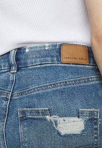 Jeansshorts i ljusblått, med en slitna bakficka och en brun läderetikett pr äglad med "AMERICAN EAGLE."