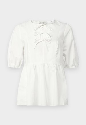 Balta blusa su trumpomis pūstomis rankovėmis, apvaliu iškirpimu ir priekyje su raišteliais. Turi smulkiai surinktą liemenį ir lygaus medvilninio audinio.