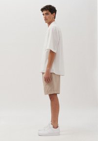 Witte korte mouwen overhemd, beige shorts en witte sneakers. Eenvoudig ontwerp met schone lijnen en neutrale kleuren. Gladde stof textuur.