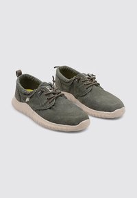 Zapatillas de lona grises con superficie texturizada, diseño de cordones, punta redonda y suela de goma. Incluyen una pestaña en la parte trasera para facilitar su colocación.