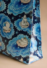 Niebieska torba w wzory z błyszczącym wykończeniem, z postaciami Moominów na ciemnym, gwiaździstym tle, z puszystymi chmurami i dekoracyjnymi gwiazdami.