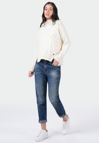 Crème-kleurige gebreide trui met een gespikkeld patroon, losse pasvorm. Gecombineerd met versleten blauwe denim jeans en witte sneakers.