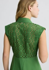 Abito verde con un design a colletto, caratterizzato da un raffinato motivo ad occhio sulle spalle, tessuto testurizzato e schiena senza cuciture.