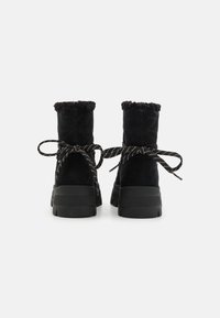 Bottines en suède noir avec une bordure en fourrure en haut, semelles en caoutchouc noir et lacets noirs et blancs à motifs noués en nœud à l'arrière.
