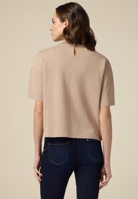 Beige kortærmet top med rund hals, der har en lille nøglehul detalje bagpå og en tekstureret stof. Sammen med mørke jeans.