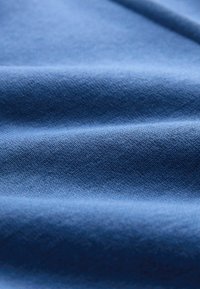 Zachte blauwe stof met zichtbare fijne weefstructuur en zachte plooien die een textuur creëren met subtiele schaduwen en highlights.