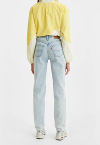 Jeans de tiro alto en azul claro con un corte recto, que cuentan con bolsillos traseros y una etiqueta de cuero marrón. Combinados con un top corto amarillo.