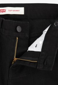 Jeans skinny Levi's 510 negros con una cremallera dorada abierta y una tela interior blanca visible y botón.