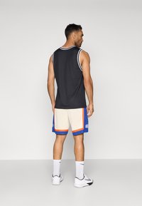 Melnas bez piedurknēm sporta jersey ar baltu apdari, kopā ar krēmkrāsas šortiem, kuru malu rotā zili un oranži svītri. Valkāts ar baltām zeķēm un apaviem.