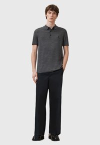 Graues Poloshirt aus strukturiertem Stoff, mit kurzen Ärmeln und Kragen, kombiniert mit dunklen Hosen und schwarzen Schuhen. Einfaches Design mit minimalen Details.