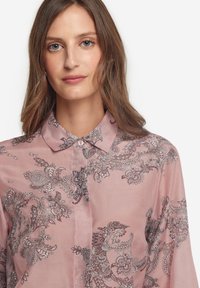 Ljusrosa blus med blommönster och paisleymönster i grått, med krage och knappstängning. Tillverkad av ett smidigt, glänsande tyg.
