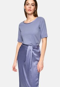 Light purple top with short rolled sleeves, paired with a shinier, darker purple satin skirt that features a waist tie detail.