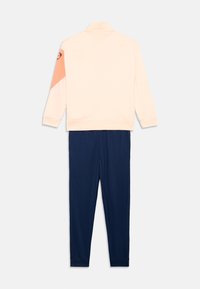 Trainingjack in lichtroze met een oranje accent, gecombineerd met marineblauwe broek. Beschikt over een hoge kraag en ribgebreide manchetten. Zachte stof.