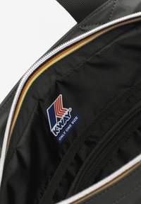 Sac à dos en tissu noir avec une ouverture zippée, doté d'une doublure rayée colorée et d'une étiquette logo K-Way à l'intérieur. Texture lisse, design durable.