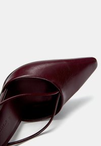 Escarpin en cuir bourgogne avec un bout pointu, présentant un design élégant et des fines lanières à la cheville. Texture lisse avec une finition brillante.