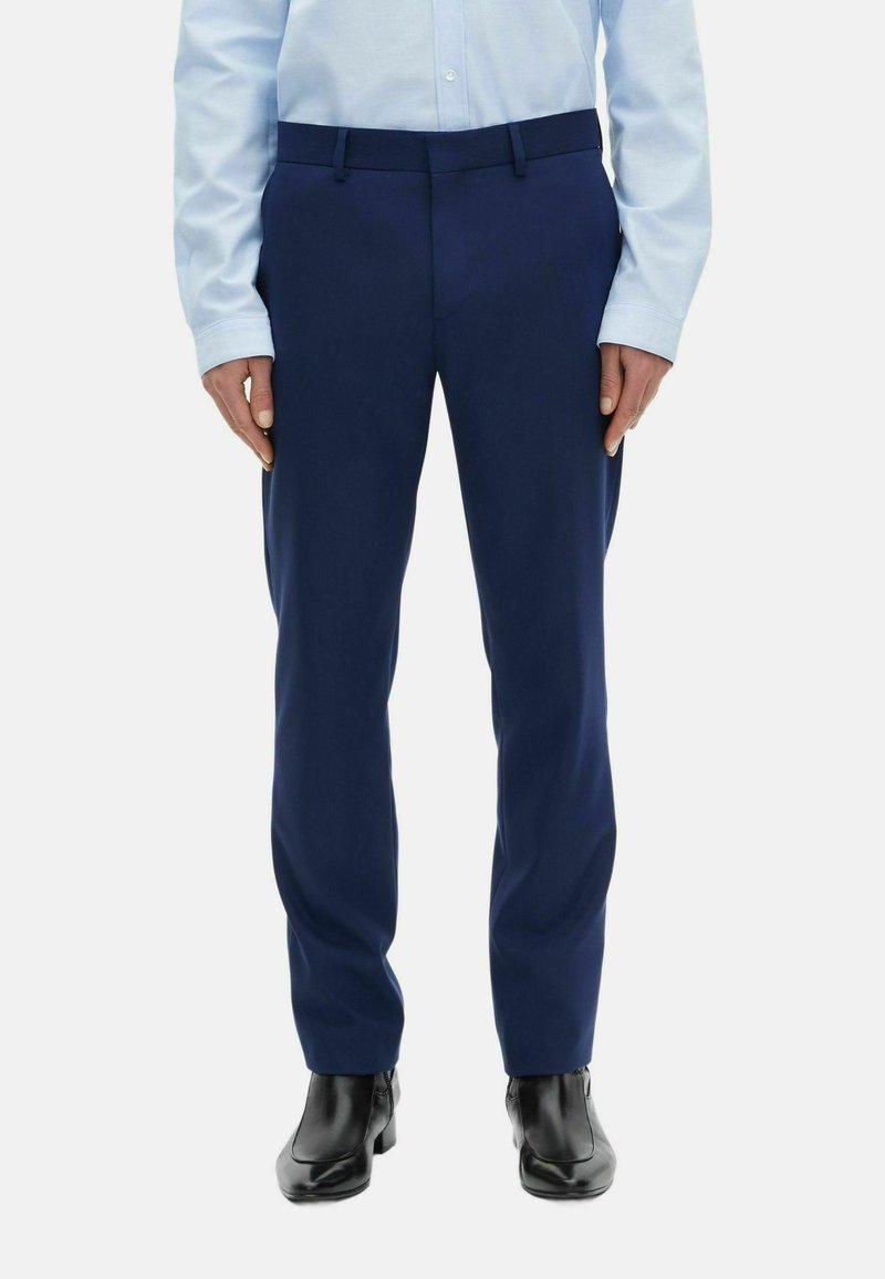 Marineblau maßgeschneiderte Hose mit glatter Textur, ausgestattet mit einem Standardbund und einer vorderen Bügelfalte, kombiniert mit schwarzen Anzugschuhen.